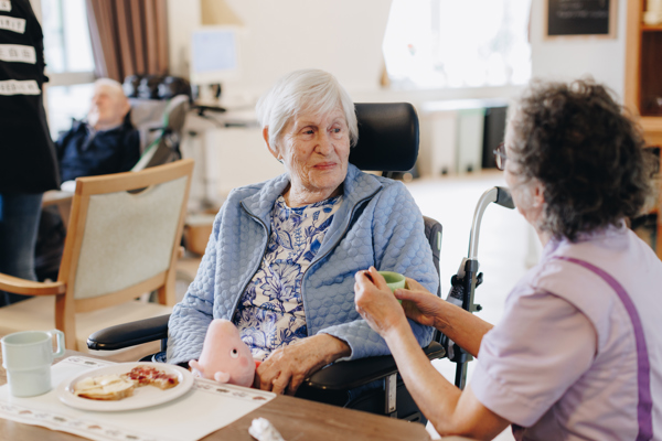 De Waterpoort Zorgpartners Bewoner Medewerker Eten Helpen Bord Tafel Rolstoel Interactie